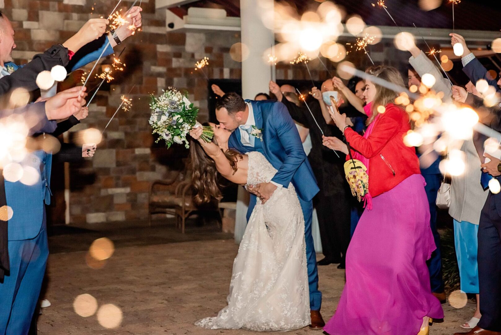A Bride and Groom Kissing With Guests Holding Crackers