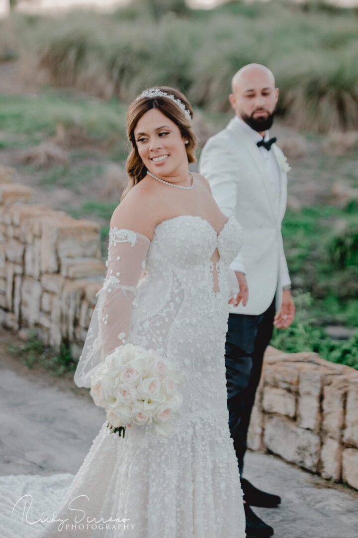 A bride and groom walking on the side of a bridge.