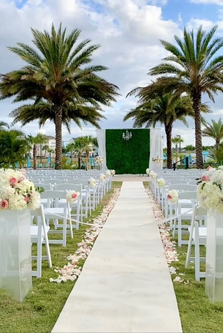 A wedding ceremony with white chairs and palm trees.